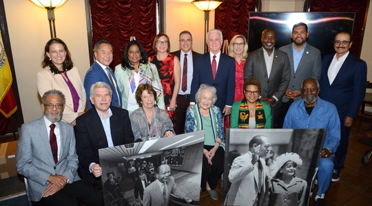 Councilmembers past and present pose with Mayor Bass and large photographs of Mayor Bradleyy
