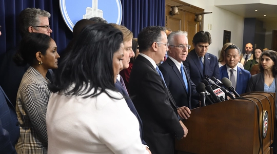 Councilmember assemble around lectern in Council media Room, Council President Krekorian at microphone.