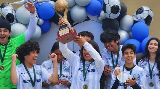 Young boy and girl soccer players hold trophy cup aloft, celebrating a tournament victory.