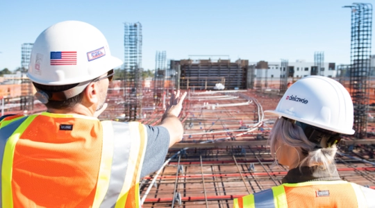 Engineers in hardhats and safety vests looing over massive construction site