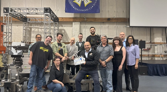 Councilmember Nazarian seated with production slate (clapper) surrounded by members of IATSE 80, under a banner with the IATSE 80 logo.