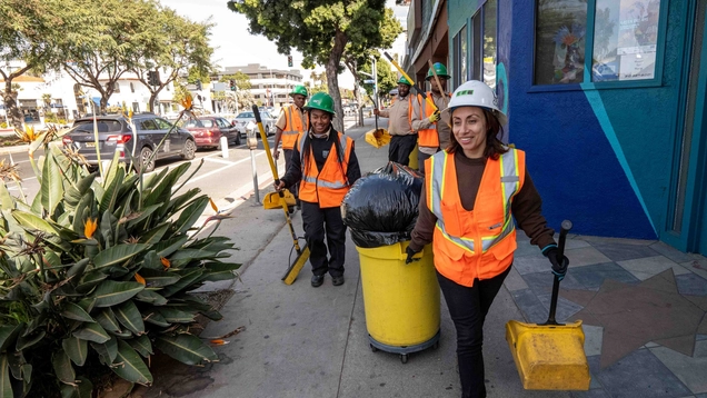 Los Angeles Conservation Corps members carrying cleaning supplies on a busy sidewalk