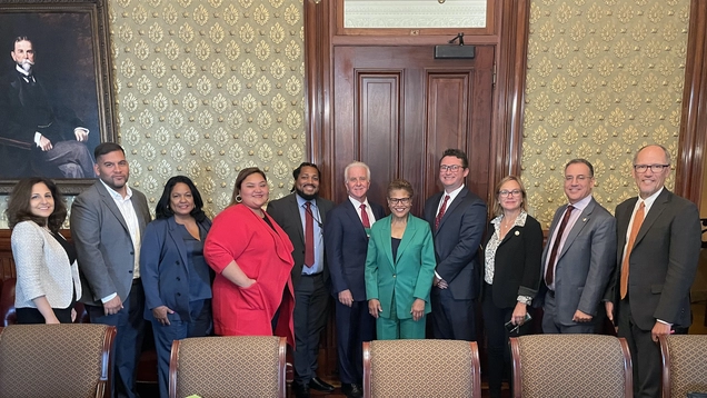 Councilmembers and Mayor pose for photo with Neera Tanden and Tom Perez in conference room of Eisenhower Executive office Building. 