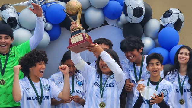 Young boy and girl soccer players hold trophy cup aloft, celebrating a tournament victory.