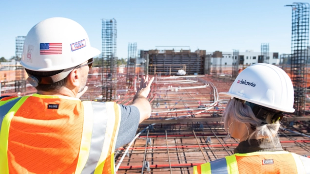 Engineers in hardhats and safety vests looing over massive construction site